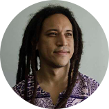 Foto de Marcos Levi, gestor do Centro Cultural Bom Jardim. Levi é um homem negro, usa dreads. Ele está com uma blusa estampada roxa e branca. Ele olha para o lado.