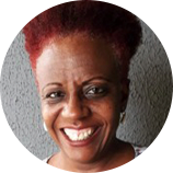 Foto de Vera Rodrigues, que compõe o conselho de administração do IDM. Vera é uma mulher negra, possui cabelos crespos, ruivos e sorri em direção a fotografia.