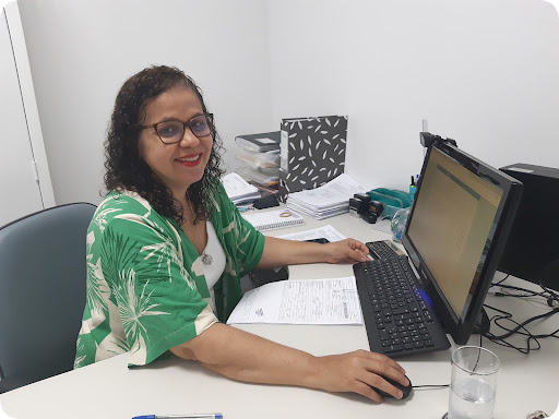 Foto de colaboradora do IDM sentada em seu local de trabalho de frente para o computador.