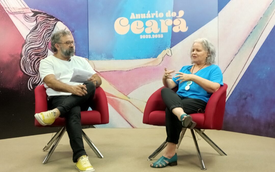 Foto de entrevista em que aparece a presidenta do IDM, Rachel Gadelha. O jornalista que a entrevista é Jocélio Leal. Ambos estão sentados em cadeiras vermelhas e ao fundo lê-se: Anuário do Ceará 2022-2023.
