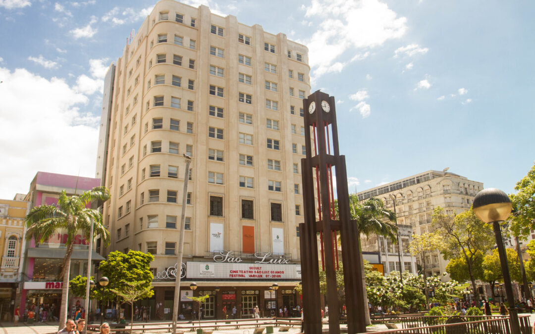Foto da fachada do Cineteatro São Luiz. É possível ver parte da Praça do Ferreira, onde fica localização do Cineteatro. É possível ver o relógio alto e característico do local.