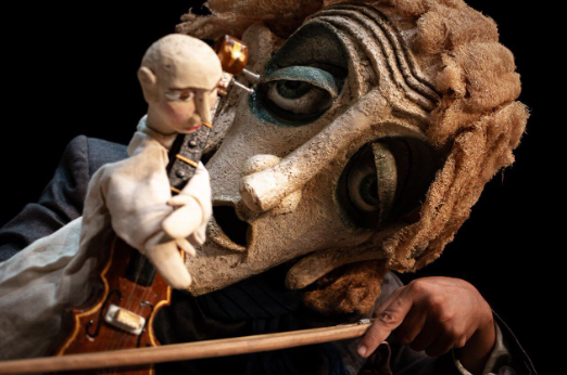 foto de máscara teatral e um boneco de teatro, dentre eles: violino, mão, boneco e máscara