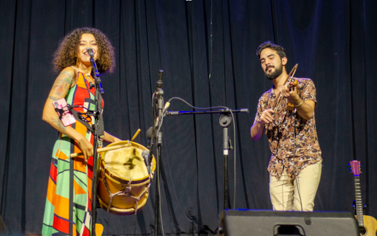 Card com fotos com duas pessoas. Uma mulher, que toca uma tambor enquanto cantar e um homem que toca violino.