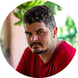 Foto de Giusevilly de Souza Mello. Homem jovem, com poucos cabelos grisalhos. Usa blusa na cor vermelha.