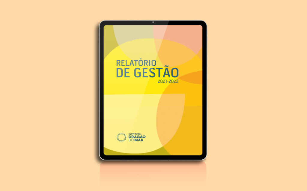 Uma simulação de tela de tablet reproduz a capa em amarelo e laranja onde se lê: "do Relatório de Gestão 2021/2022".  Abaixo, no canto inferior esquerdo, a logo do Instituto Dragão do Mar em verde.