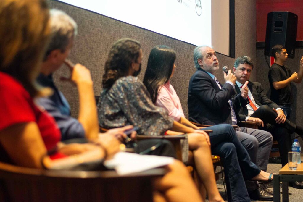 Homens e mulheres, brancos, roupas em cores diversas, debatem em cadeiras lado a lado.