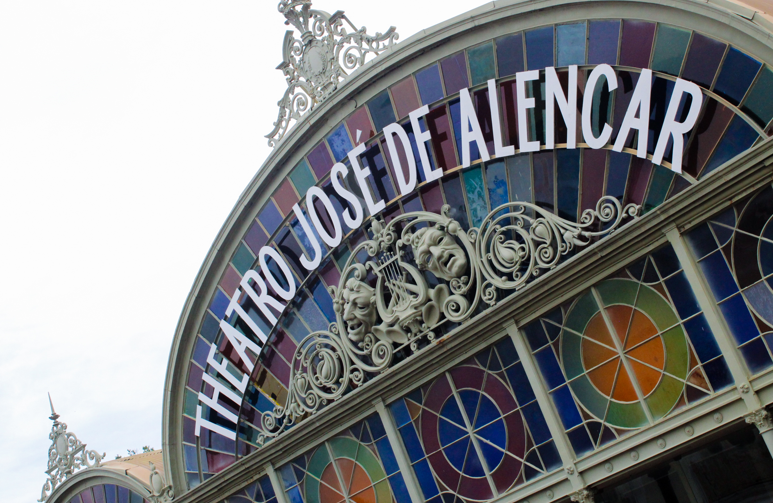 Parte superior da fachada do Theatro Jospe de Alencar com vitrais coloridos e letreiro com cores brancas