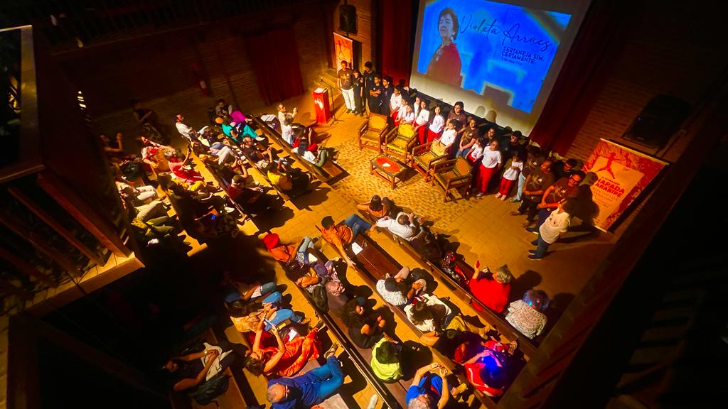 Em um auditório lotado, crianças cantam no palco.