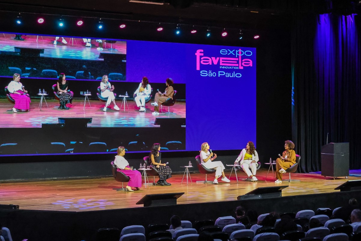 Foto de programação da Expofavela 2022. É possível ver 5 convidadas palestrando. Atrás um telão mostra as convidadas.