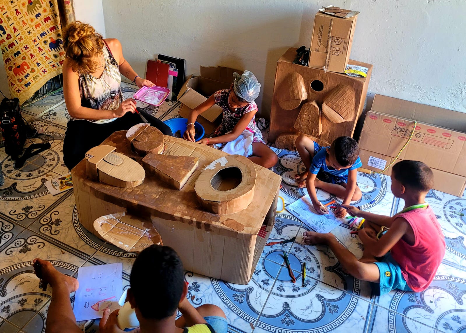 Imagens de crianças com folhas na mão. Elas estão sentadas no chão, em círculo.