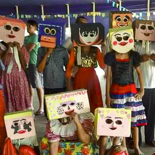 Crianças e adolescentes de roupas coloridas e máscaras quadradas e coloridas feitas a partir de caixas de papelão posam para a foto.