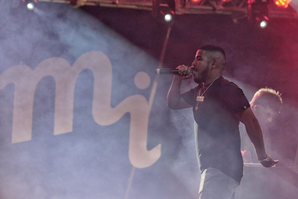 Artista se apresenta em um palco iluminado, cantando ao microfone em meio a efeitos de fumaça durante o Festival MI.